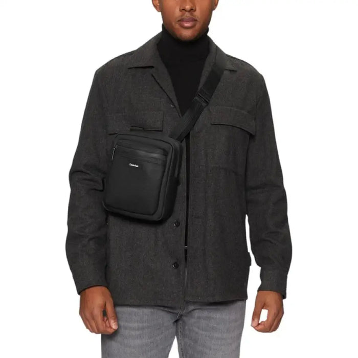 Black crossbody bag paired with dark turtleneck and utility jacket by Calvin Klein