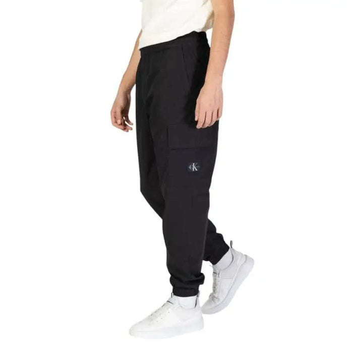 Black jogger sweatpants with elastic cuffs paired with white sneakers by Calvin Klein Jeans