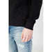 Black knit sweater sleeve beside light blue distressed jeans from Calvin Klein Jeans