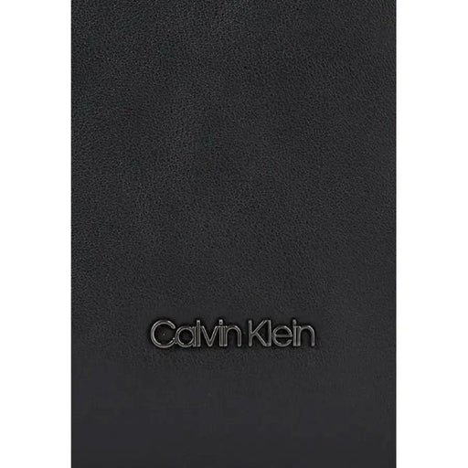 Black leather surface featuring embossed Calvin Klein logo on a men’s bag