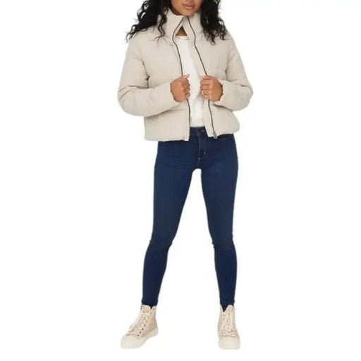 Cream-colored puffer jacket styled with dark skinny jeans and beige sneakers by Only