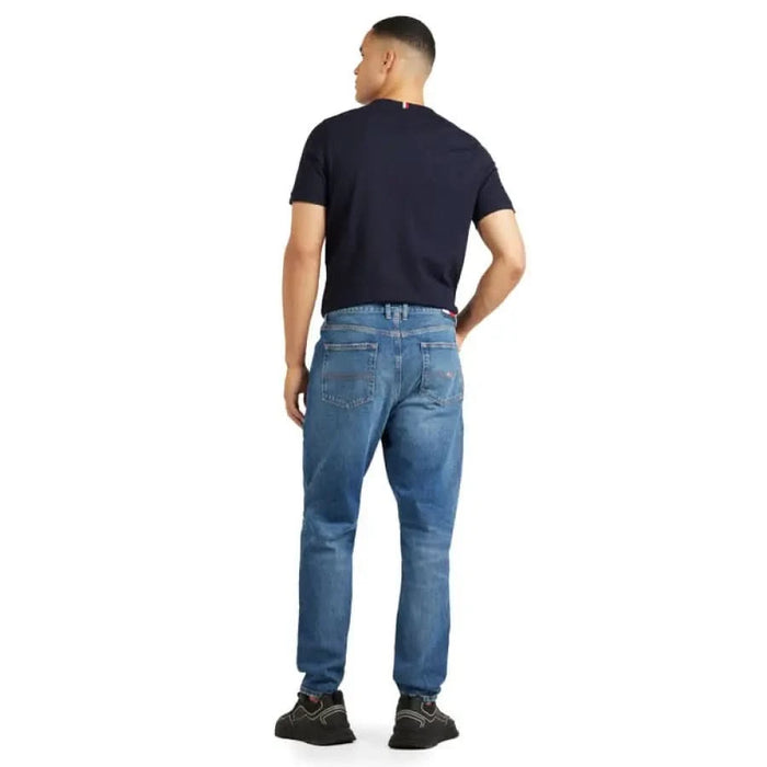 Man in blue jeans and black t-shirt from behind, showcasing Tommy Hilfiger Jeans