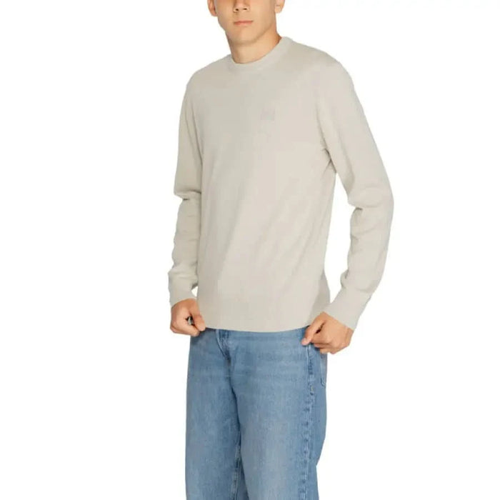 Man in light-colored long-sleeved sweater and blue jeans from Boss Men Knitwear