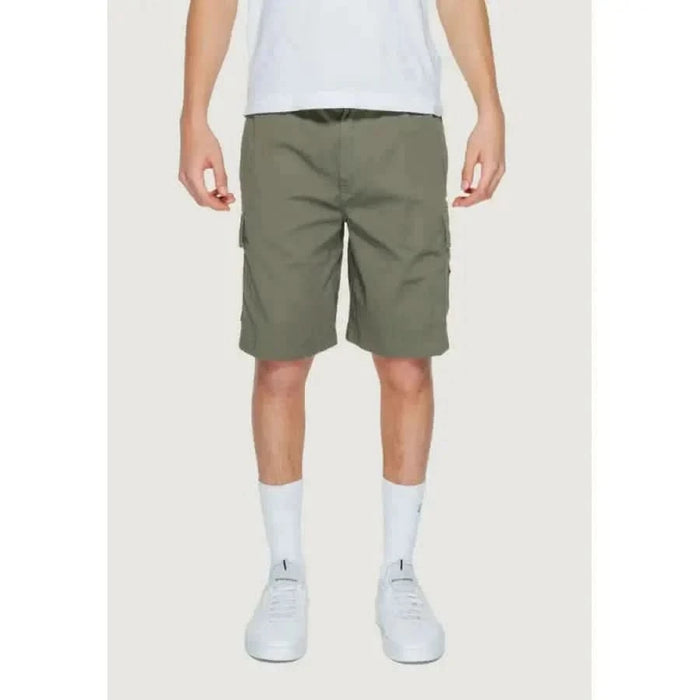 Person in Calvin Klein olive green cargo shorts with white shirt and sneakers