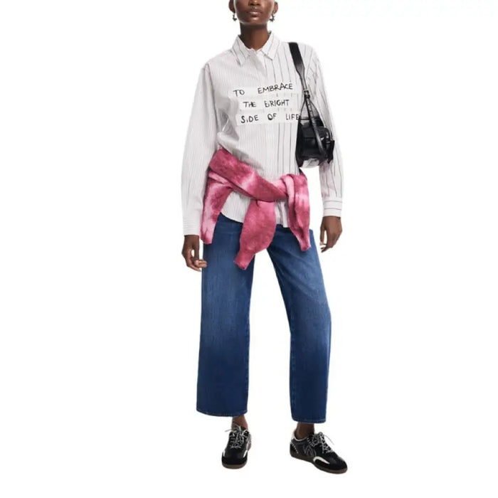 Person in a white Desigual shirt, blue jeans, and pink sweater tied at the waist