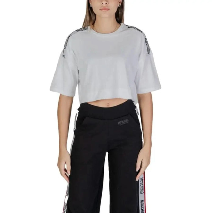 Person in a white cropped Moschino Underwear T-shirt and black track pants with stripes