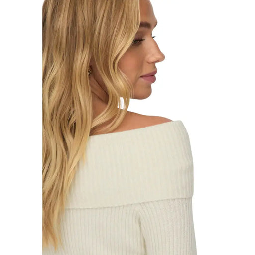 Profile view of a woman with long blonde hair in an off-shoulder white sweater