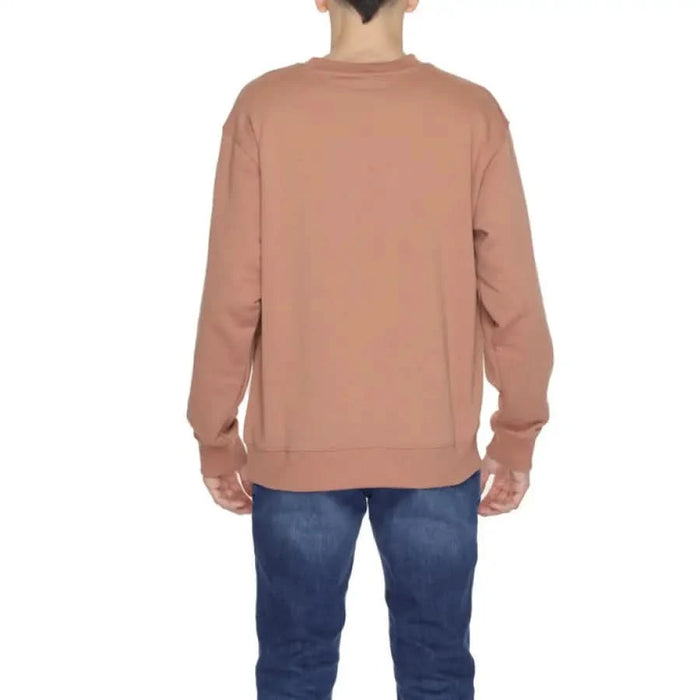 Back view of man wearing salmon-colored crewneck sweatshirt with blue jeans by New Balance