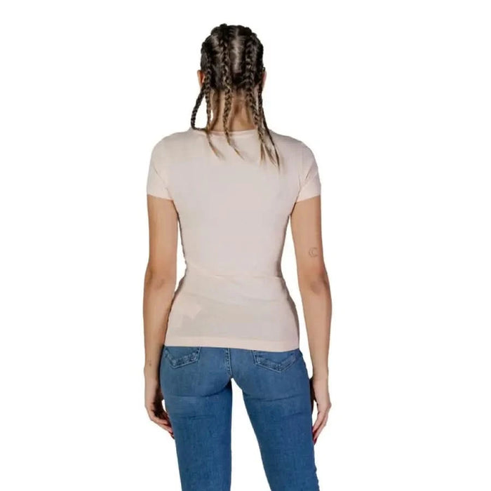 Back view of an individual in a Guess Women T-Shirt, beige with blue jeans and braided hair