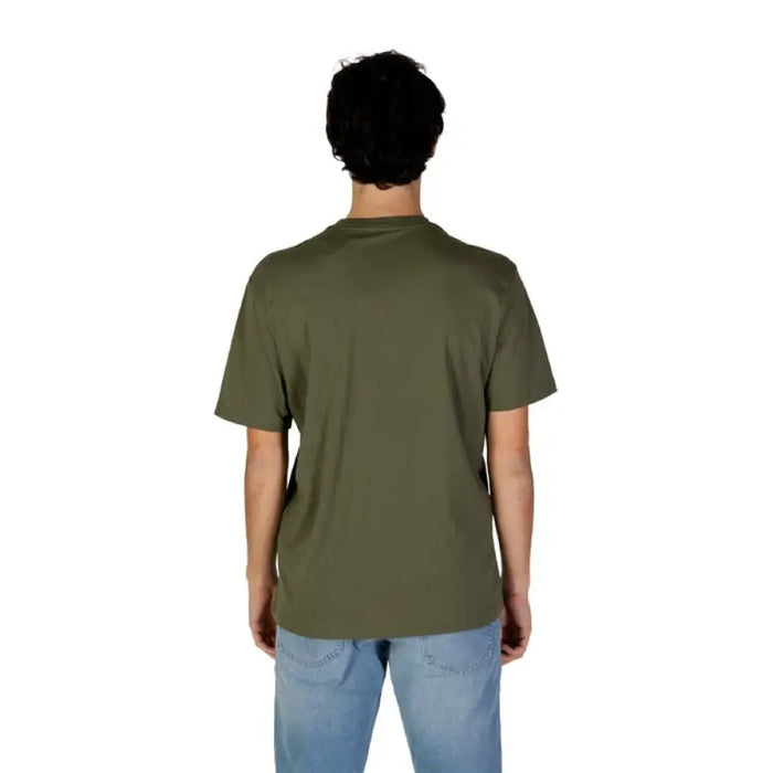 Back view of a man in an olive green Gas T-shirt and blue jeans