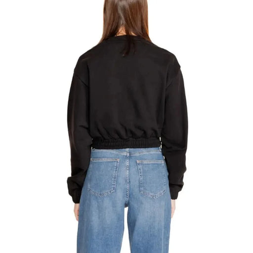 Back view of a person in a black cropped Calvin Klein sweatshirt and blue jeans