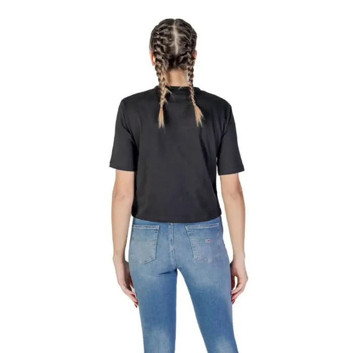 Back view of a person in a black Guess Active t-shirt and blue jeans with braided hair