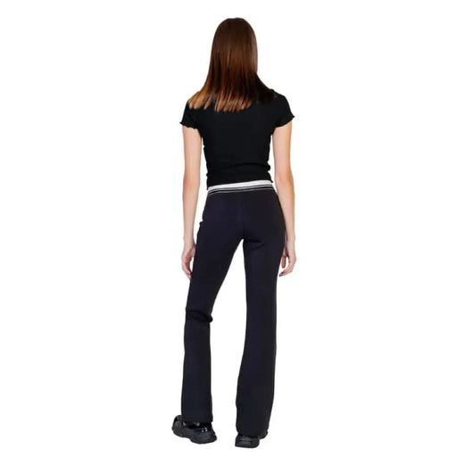 Back view of a person in black t-shirt and dark flared pants from Guess Active