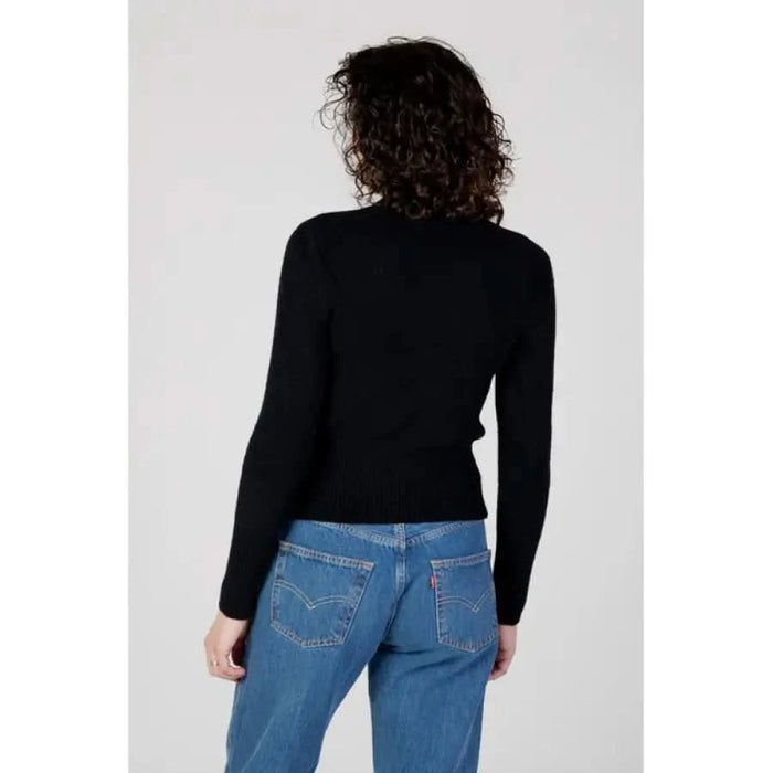 Back view of a person in a black long-sleeved top and blue jeans - Guess Women Knitwear