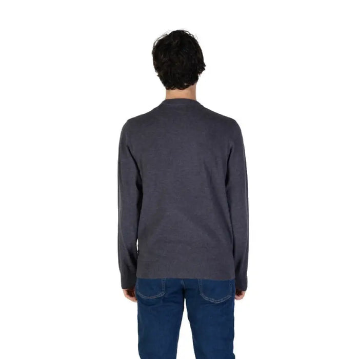 Back view of a man in a dark gray sweater and blue jeans showcasing a knit sweater