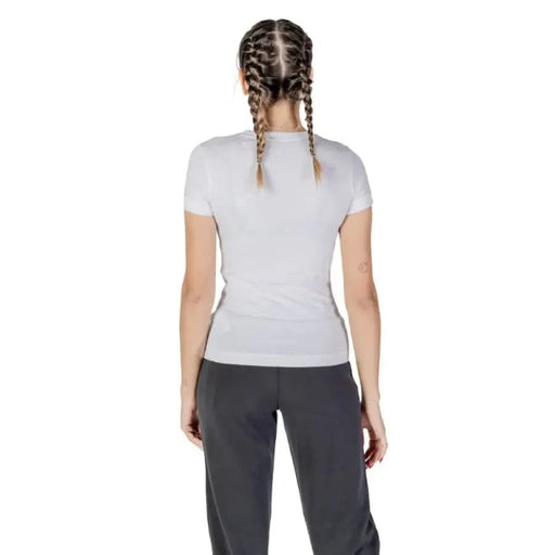 Back view of a person in a Guess Women T-Shirt with braided hair and dark pants