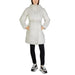 White belted winter coat with hood over black pants and sneakers by Calvin Klein Jeans