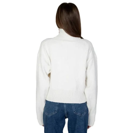 Model wearing Calvin Klein women’s white turtleneck sweater with blue jeans, back view