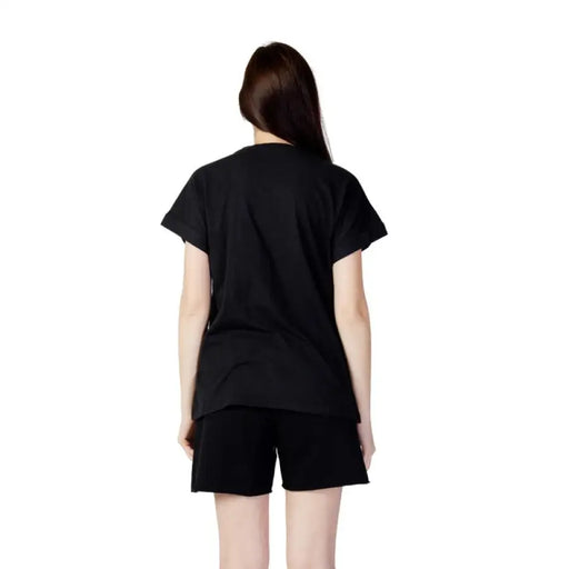 Woman in a black Blauer T-shirt and shorts, viewed from behind