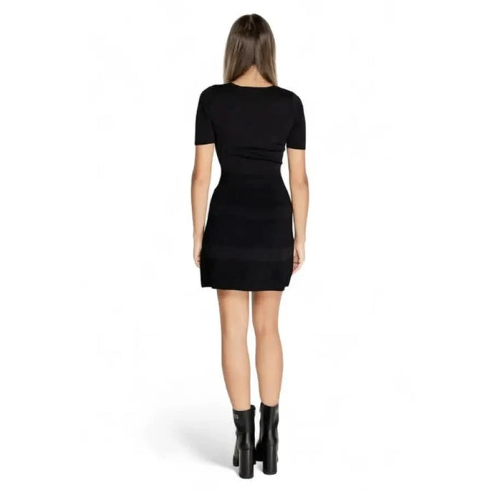 Woman in a short black dress and ankle boots from Morgan De Toi, viewed from behind