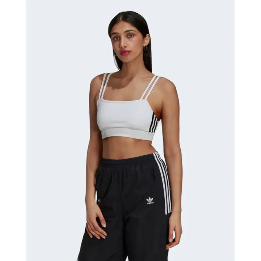 
                      
                        Woman in white Adidas sports bra and black track pants with signature stripes
                      
                    